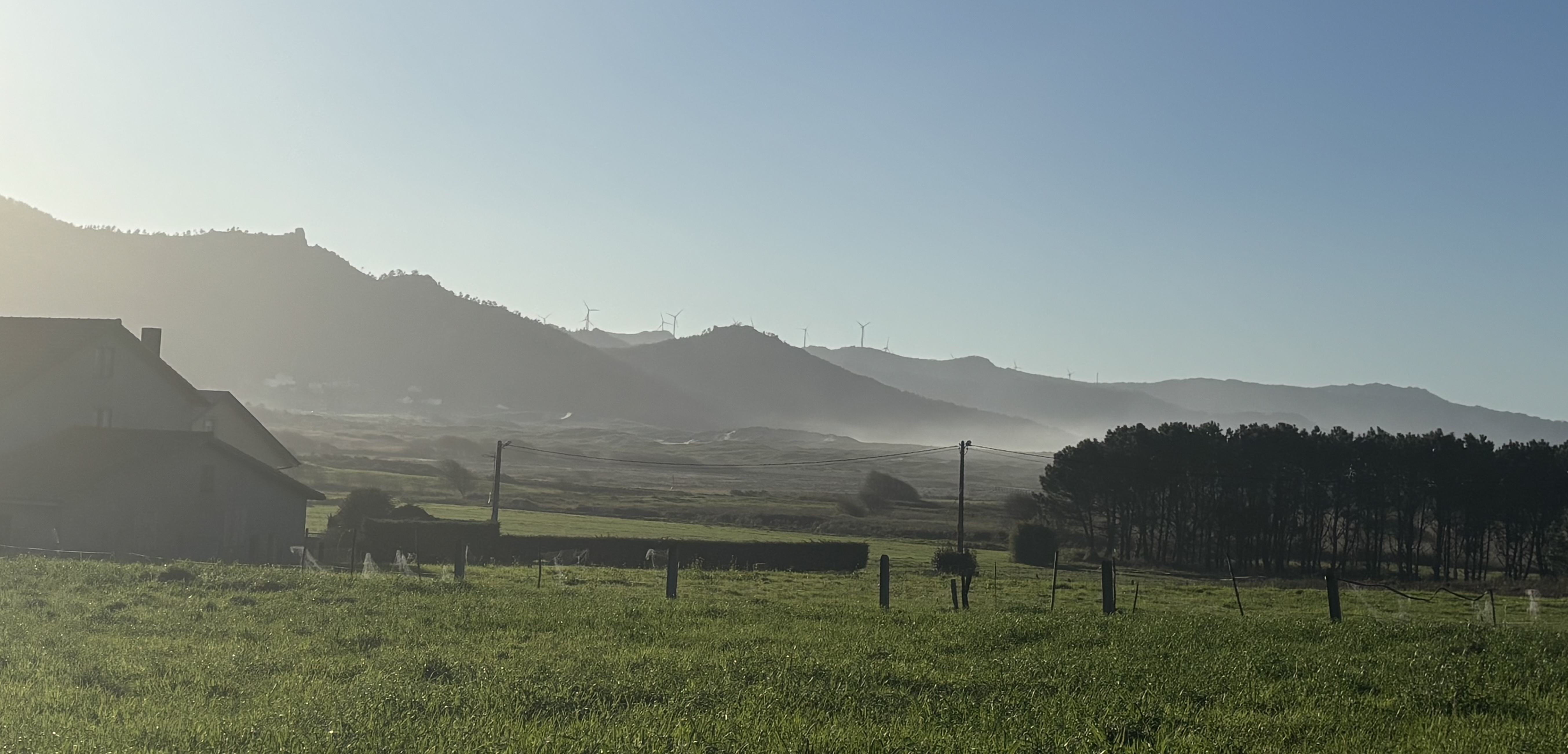 Open field with distant mountains and wind turbines at dusk